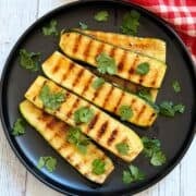 Grilled zucchini is served on a plate, garnished with cilantro.