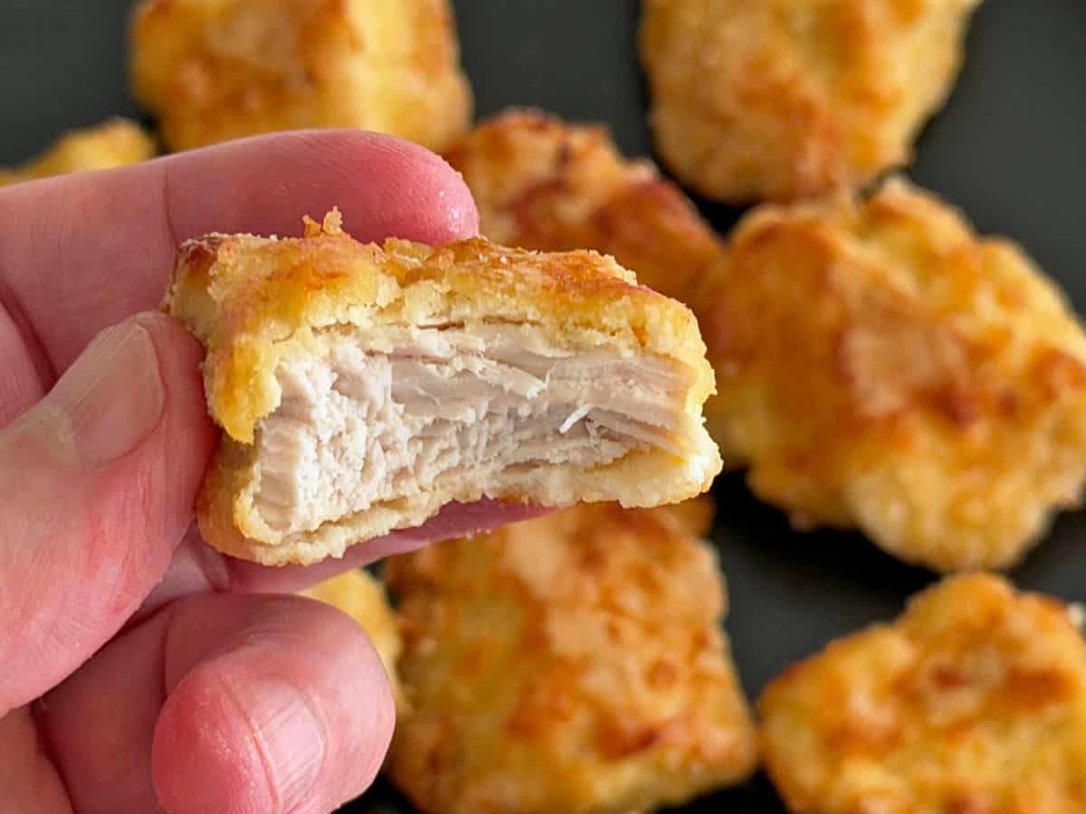 A hand holds a bitten chicken nugget.
