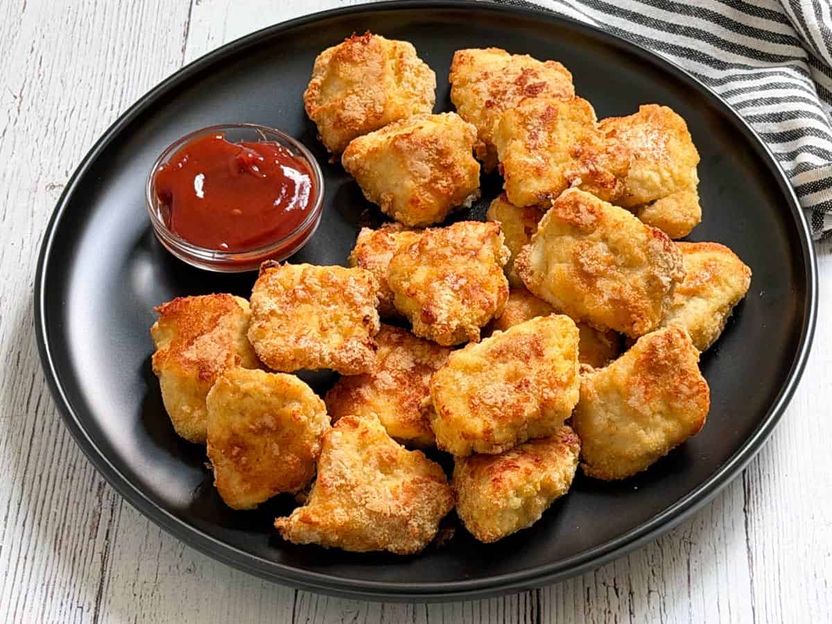 Keto chicken nuggets are served on a dark plate with ketchup.