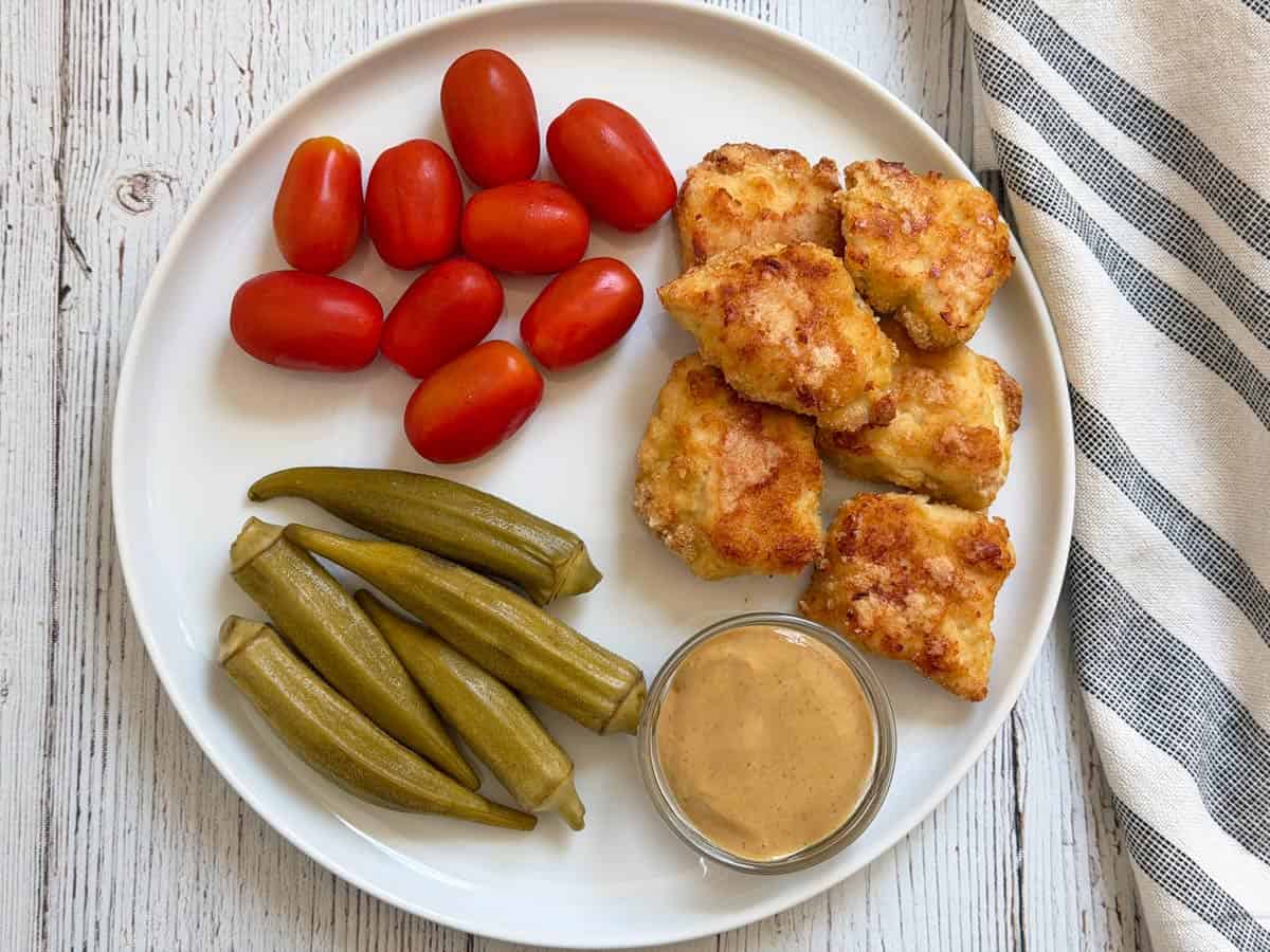 Keto chicken nuggets leftovers are served with tomatoes, pickles, and mustard.