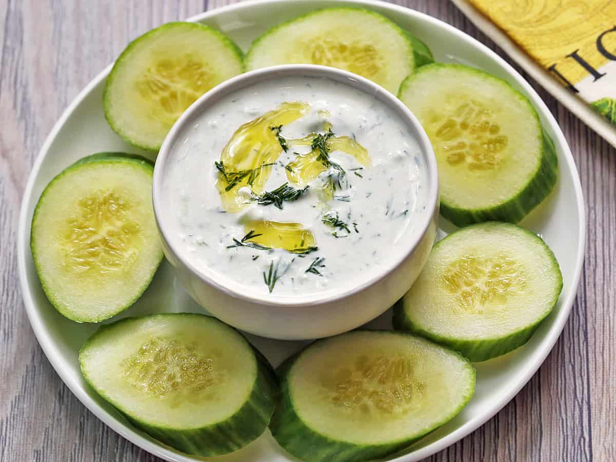 Tzatziki sauce is served with sliced cucumbers.